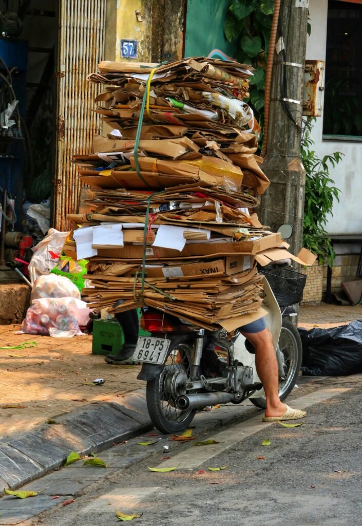 Motorbike in Hanoi carrying a large stack of recycled cardboard on a sunny day.