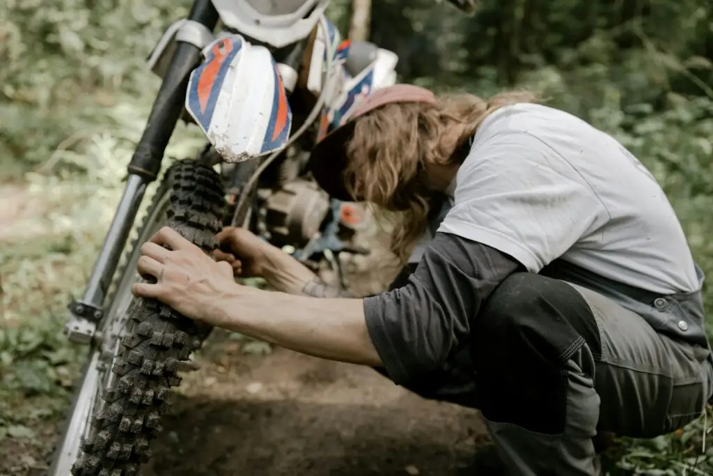 A man with long hair works on a motorcycle tire, showcasing outdoor maintenance skills.